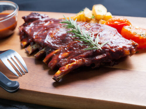 Pork,spareribs,with,tomato,and,fried,potatoes,on,wooden,plate